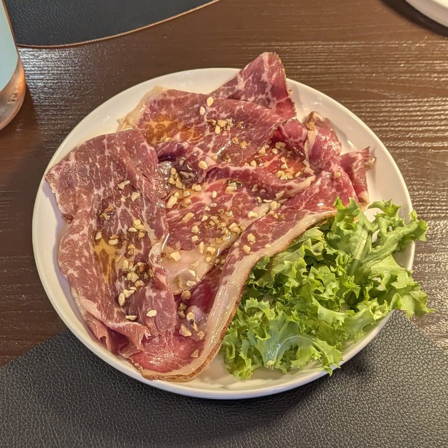 Carpaccio di Black Angus con granella di noci e olio al tartufo, con un ciuffo di insalata riccia, su un piatto bianco