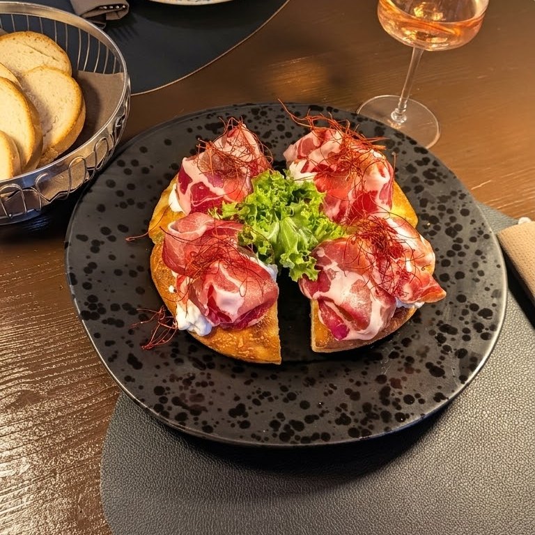 Pizza in padellino tagliata a spicchi con stracciatella, capocollo di Martina Franca e fili di peperoncino, su un piatto nero a pois
